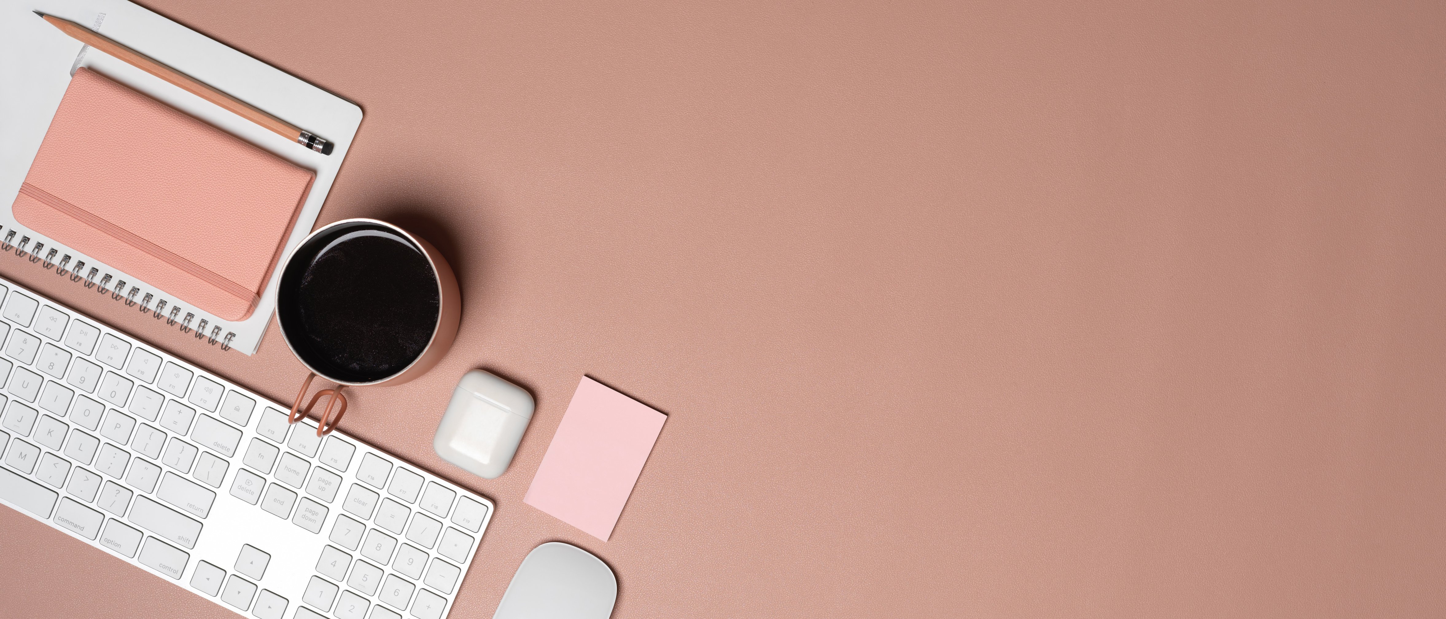 Workspace with computer keyboard, diary book, mug, accessories and copy space on pink table